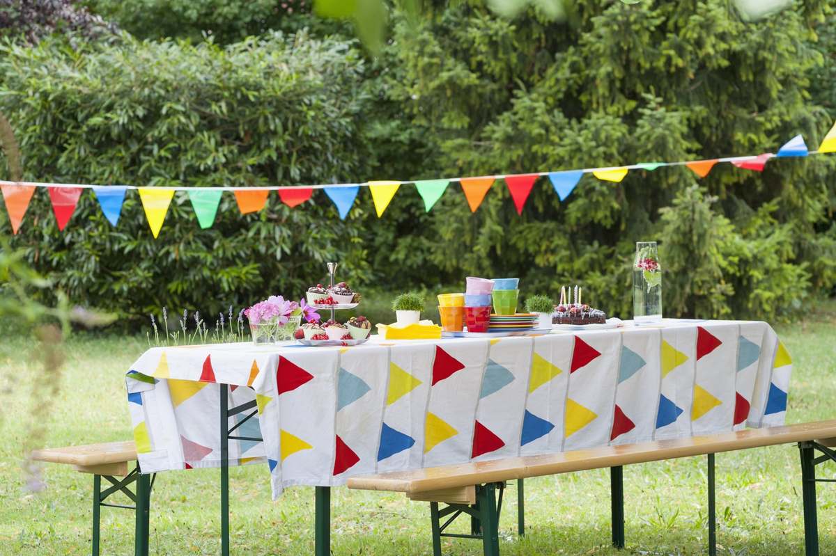 Mesa larga decorada al aire libre para un cumpleaños, con guirnaldas de colores